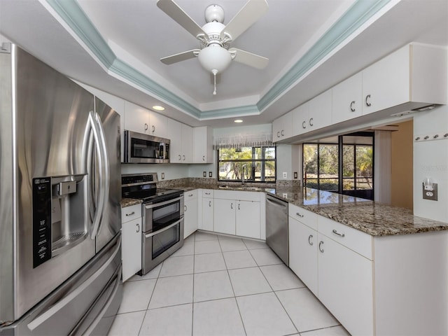 kitchen with white cabinetry, stainless steel appliances, kitchen peninsula, dark stone counters, and a tray ceiling