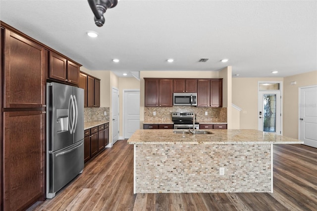 kitchen featuring light stone countertops, appliances with stainless steel finishes, tasteful backsplash, dark wood-type flooring, and an island with sink