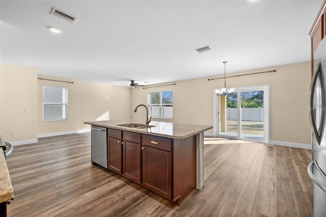 kitchen featuring appliances with stainless steel finishes, a kitchen island with sink, dark wood-type flooring, sink, and decorative light fixtures