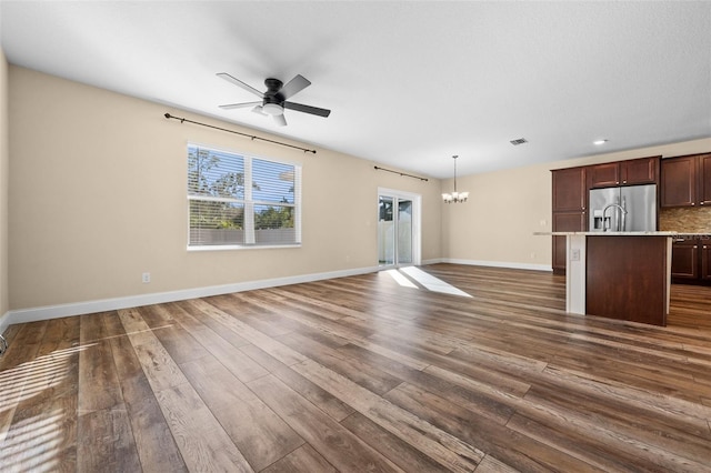 unfurnished living room with ceiling fan with notable chandelier and dark hardwood / wood-style flooring