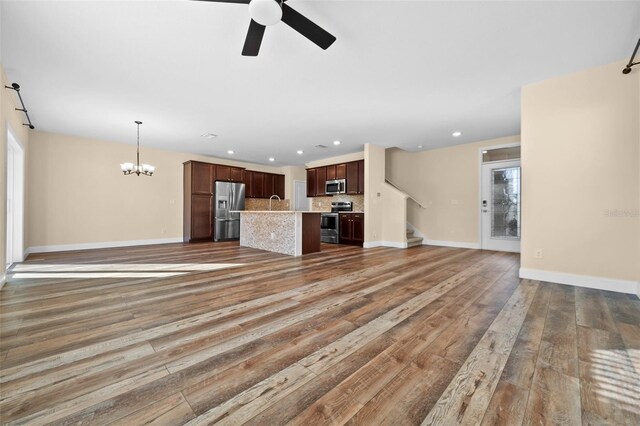 unfurnished living room with hardwood / wood-style floors, ceiling fan with notable chandelier, and sink