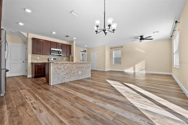 kitchen featuring light wood-type flooring, backsplash, light stone counters, ceiling fan with notable chandelier, and hanging light fixtures