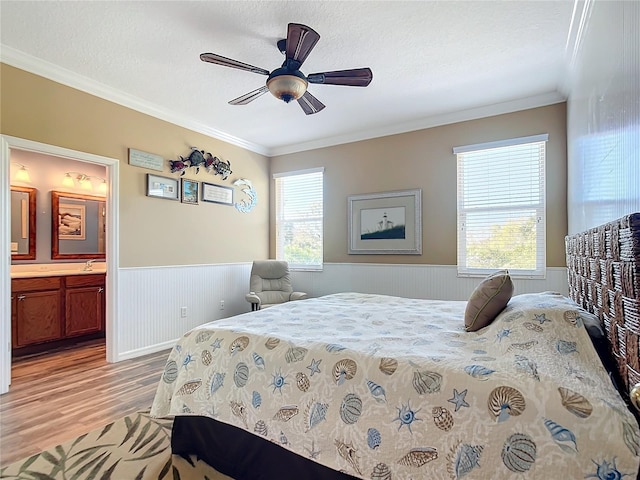 bedroom with a wainscoted wall, ornamental molding, a textured ceiling, ensuite bath, and light wood-type flooring