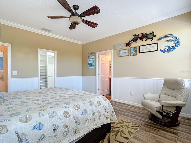 bedroom with ceiling fan, a spacious closet, wood-type flooring, a textured ceiling, and ornamental molding