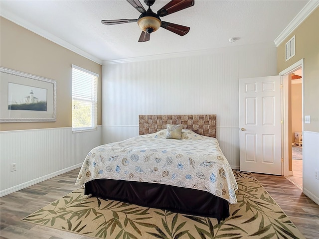 bedroom featuring ornamental molding, a ceiling fan, visible vents, and wood finished floors