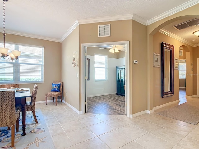 entrance foyer featuring ceiling fan with notable chandelier, light tile patterned flooring, a textured ceiling, and ornamental molding