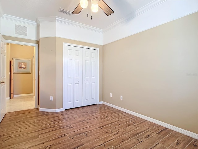 unfurnished bedroom featuring a closet, hardwood / wood-style flooring, ceiling fan, and crown molding