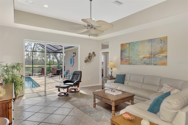 tiled living room with ceiling fan and a tray ceiling