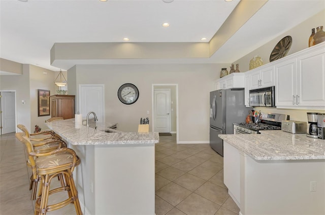 kitchen with sink, light stone counters, a breakfast bar area, white cabinets, and appliances with stainless steel finishes