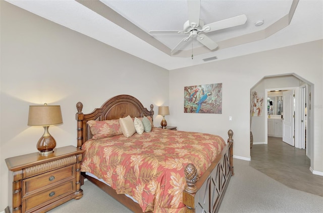 bedroom with a raised ceiling, ensuite bath, and ceiling fan