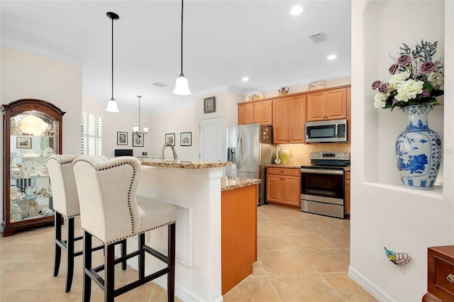 kitchen with pendant lighting, ornamental molding, an island with sink, light stone counters, and stainless steel appliances