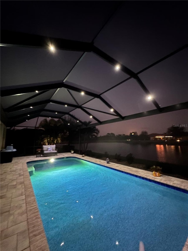 pool at twilight with glass enclosure, a water view, and a patio