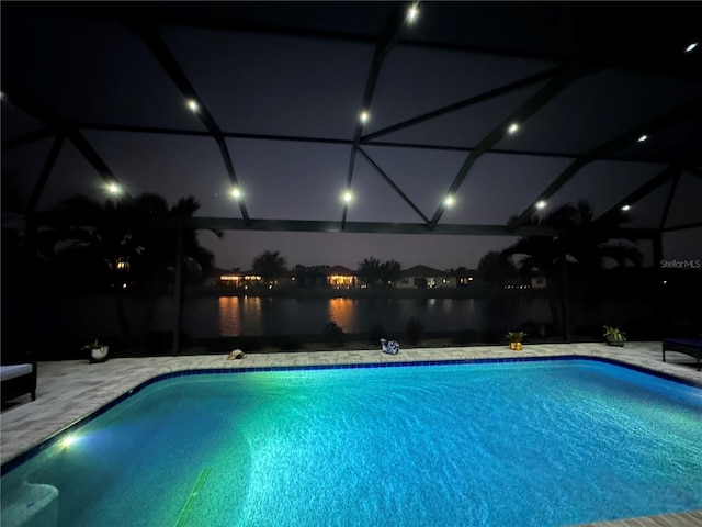 pool at twilight featuring a water view, a patio area, and a lanai