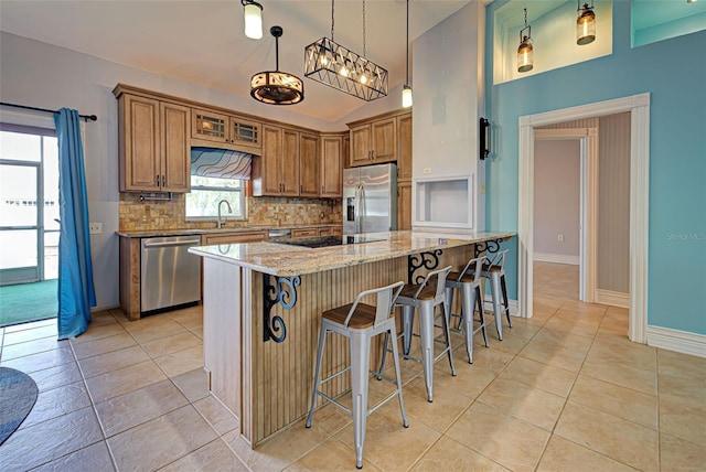 kitchen with a kitchen breakfast bar, decorative backsplash, light stone countertops, appliances with stainless steel finishes, and decorative light fixtures