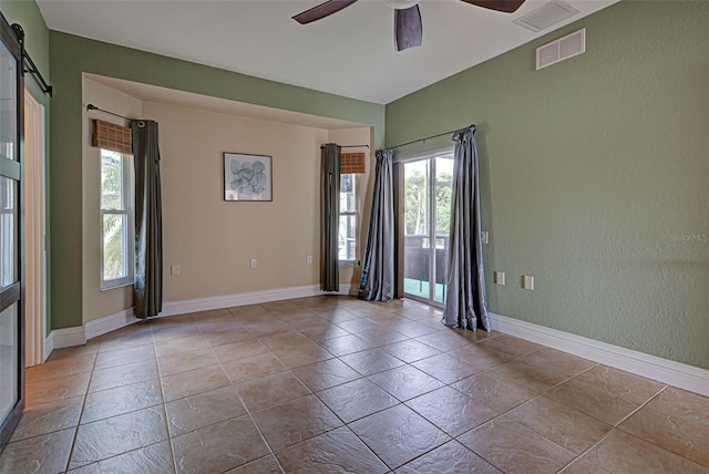 empty room featuring a barn door, ceiling fan, and a healthy amount of sunlight