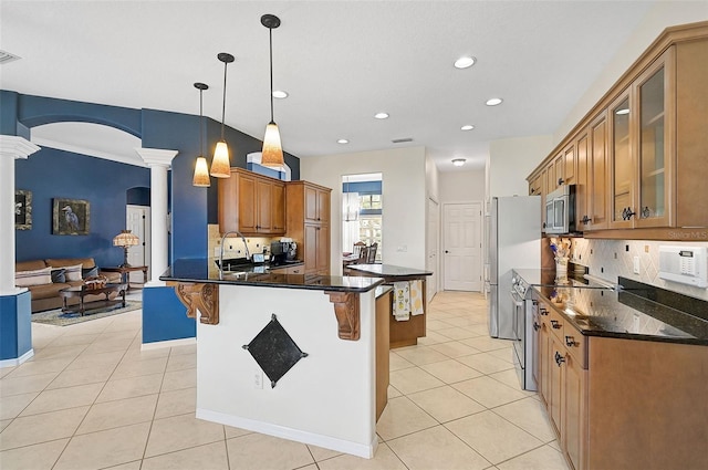 kitchen featuring decorative backsplash, appliances with stainless steel finishes, ornate columns, decorative light fixtures, and a breakfast bar area