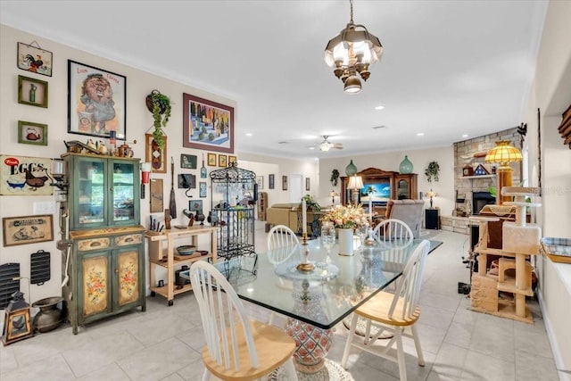 tiled dining space with ceiling fan with notable chandelier, crown molding, and a fireplace