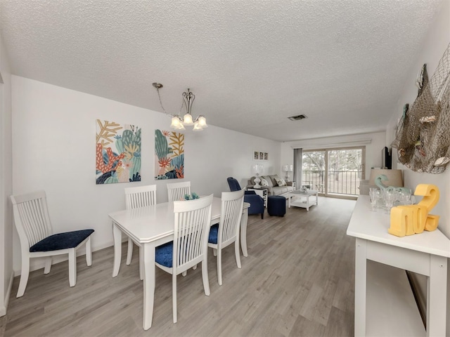 dining space with a notable chandelier, light hardwood / wood-style floors, and a textured ceiling