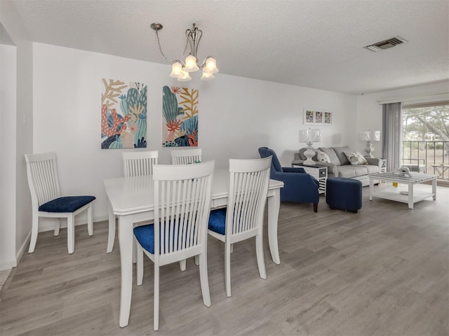 dining space with a chandelier, a textured ceiling, and light hardwood / wood-style floors