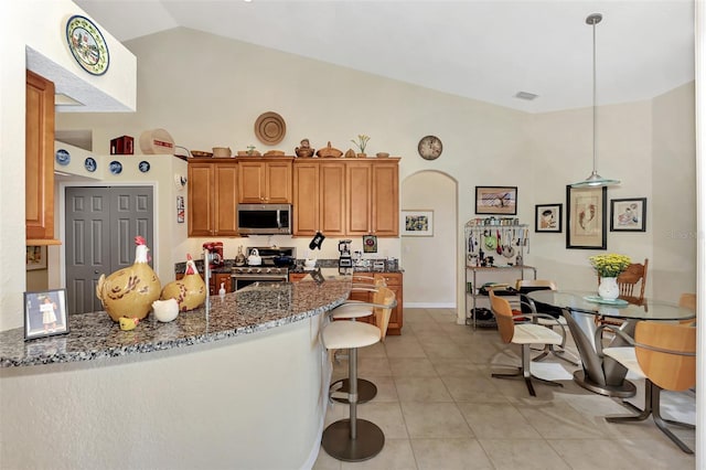 kitchen featuring kitchen peninsula, dark stone counters, stainless steel appliances, decorative light fixtures, and lofted ceiling