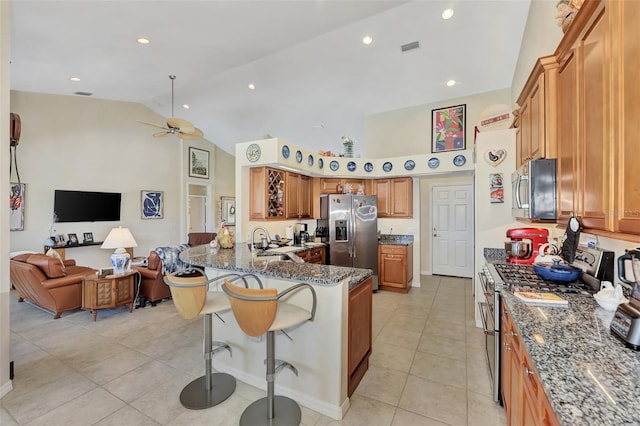 kitchen featuring appliances with stainless steel finishes, a kitchen breakfast bar, ceiling fan, sink, and dark stone countertops