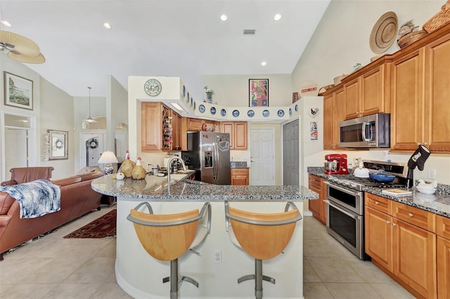 kitchen featuring stone counters, sink, stainless steel appliances, high vaulted ceiling, and a breakfast bar area