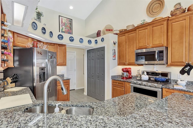 kitchen with high vaulted ceiling, sink, light tile patterned floors, light stone countertops, and appliances with stainless steel finishes