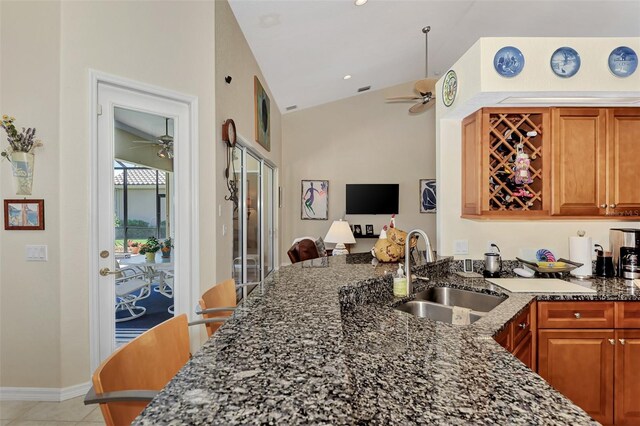 kitchen with lofted ceiling, sink, ceiling fan, dark stone countertops, and light tile patterned floors