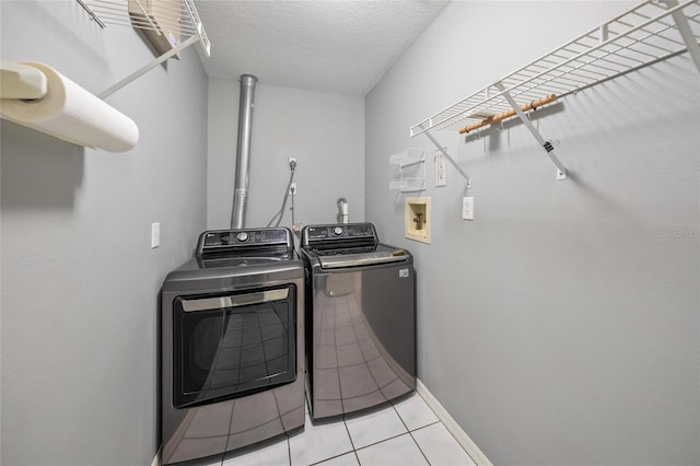 washroom with washing machine and dryer, light tile patterned flooring, and a textured ceiling