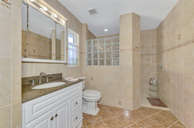 bathroom featuring vanity, tile patterned flooring, toilet, tile walls, and a tile shower