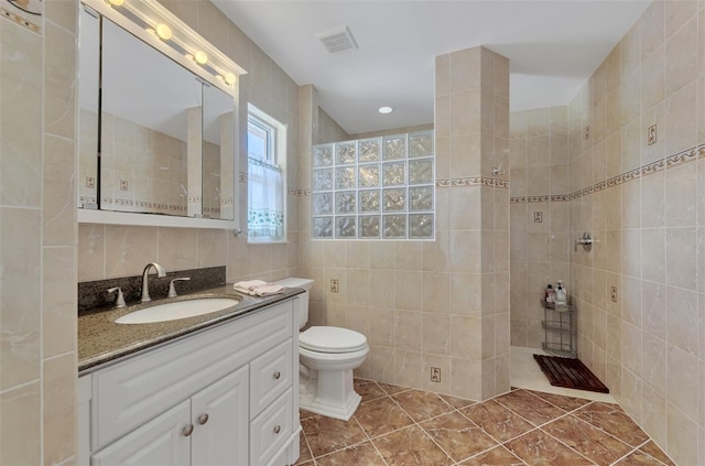 bathroom featuring vanity, tile patterned flooring, toilet, tiled shower, and tile walls