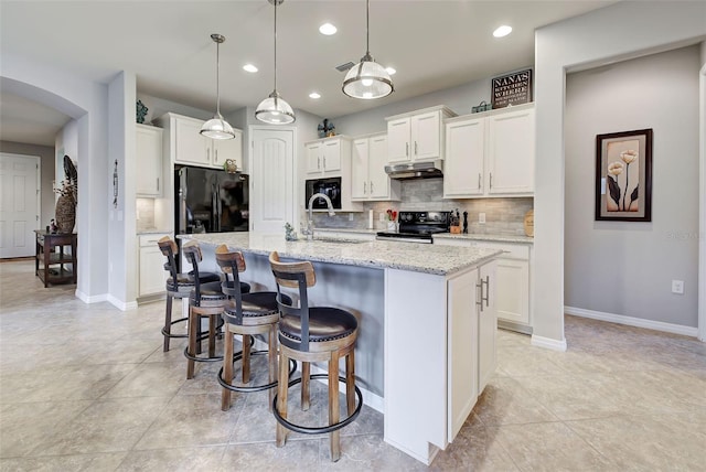 kitchen with black appliances, decorative light fixtures, white cabinetry, an island with sink, and backsplash