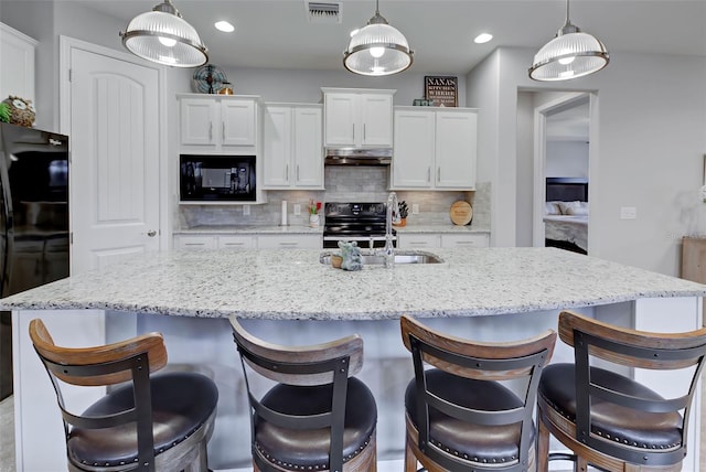 kitchen with tasteful backsplash, black appliances, an island with sink, and white cabinetry