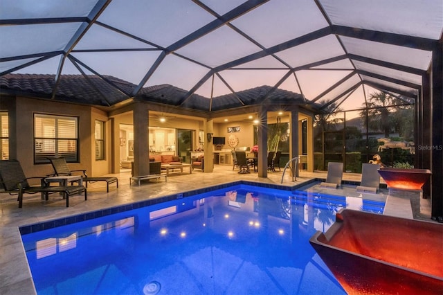 pool at dusk featuring glass enclosure, outdoor lounge area, and a patio