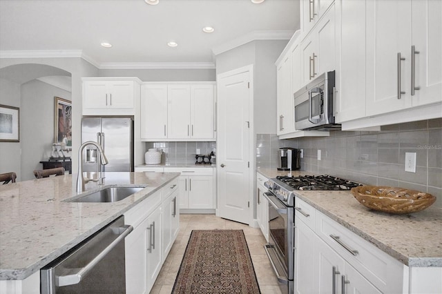 kitchen featuring stainless steel appliances, ornamental molding, a sink, arched walkways, and a center island with sink