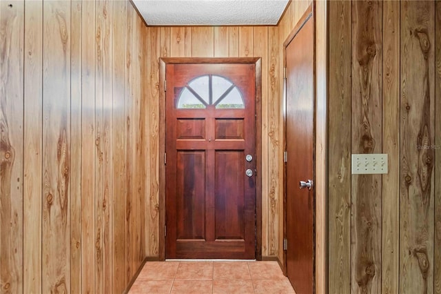 doorway with wood walls, light tile patterned floors, and a textured ceiling