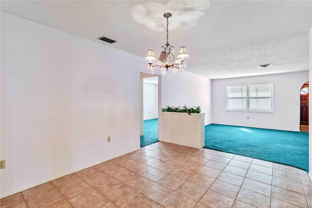 spare room featuring a textured ceiling, a notable chandelier, and light carpet