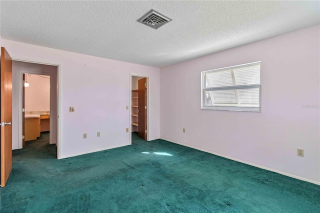 unfurnished bedroom featuring dark colored carpet, a textured ceiling, and a walk in closet