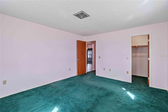 unfurnished bedroom with dark colored carpet, a walk in closet, a textured ceiling, and a closet