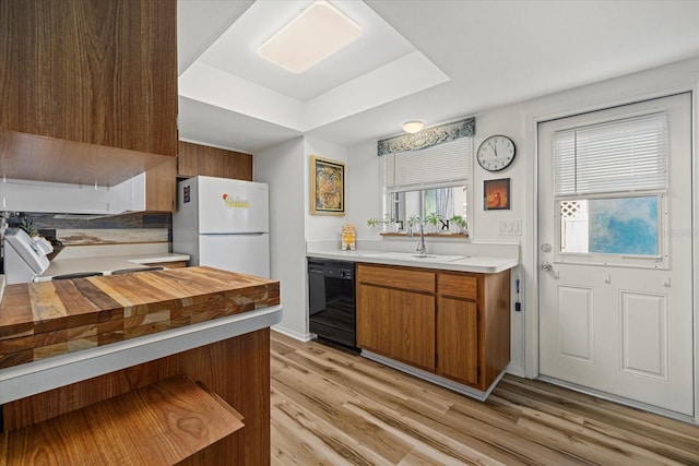 kitchen featuring dishwasher, white refrigerator, sink, light wood-type flooring, and a tray ceiling