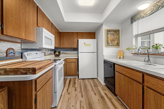 kitchen featuring a raised ceiling, light hardwood / wood-style flooring, white appliances, and sink