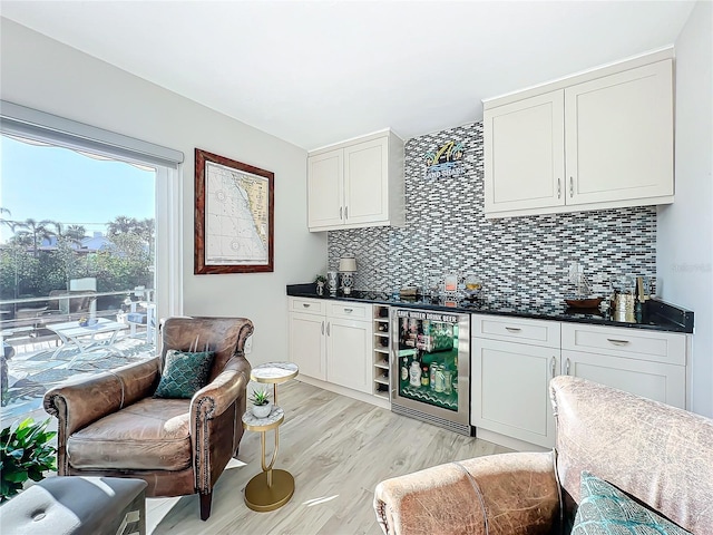 bar with light wood-type flooring, backsplash, white cabinetry, and beverage cooler