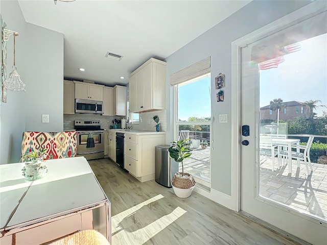 kitchen featuring sink, stainless steel appliances, tasteful backsplash, pendant lighting, and light hardwood / wood-style floors