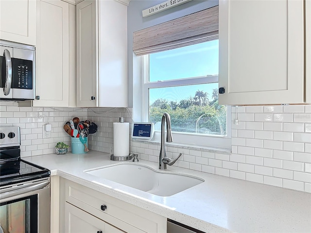 kitchen featuring sink, decorative backsplash, appliances with stainless steel finishes, light stone counters, and white cabinetry