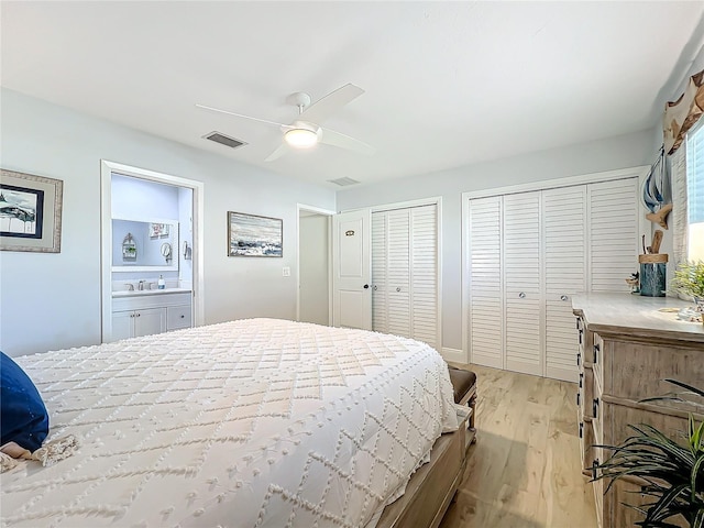 bedroom featuring ensuite bathroom, two closets, ceiling fan, sink, and light hardwood / wood-style floors