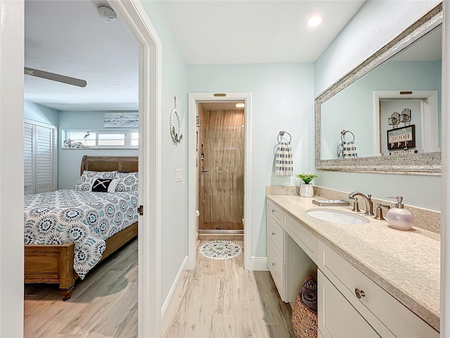 bathroom with tiled shower, wood-type flooring, vanity, and ceiling fan