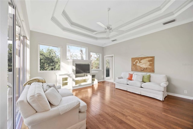 living room with hardwood / wood-style flooring, ceiling fan, crown molding, and a raised ceiling