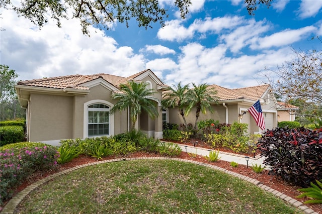 mediterranean / spanish home featuring a garage, a front lawn, a tile roof, and stucco siding