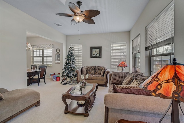 carpeted living room with ceiling fan with notable chandelier