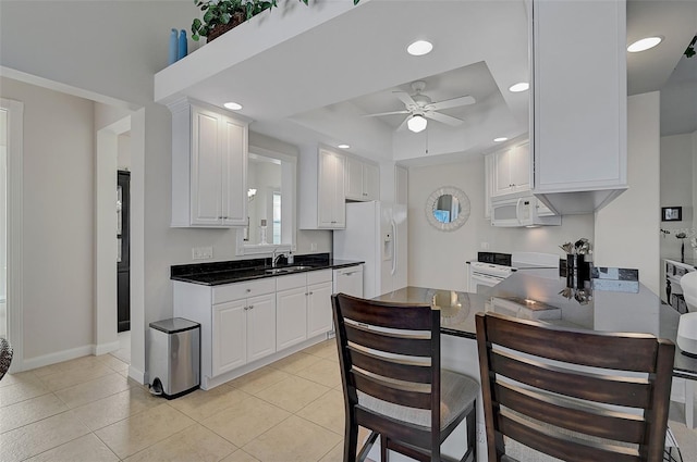 kitchen with ceiling fan, sink, a raised ceiling, white appliances, and white cabinets